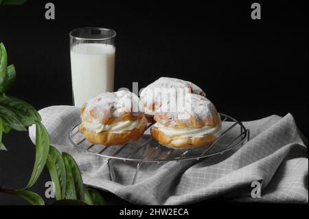 deliziose torte profiteroles eclairs su uno stand con un asciugamano fatto in casa e un bicchiere di latte fresco su sfondo nero Foto Stock