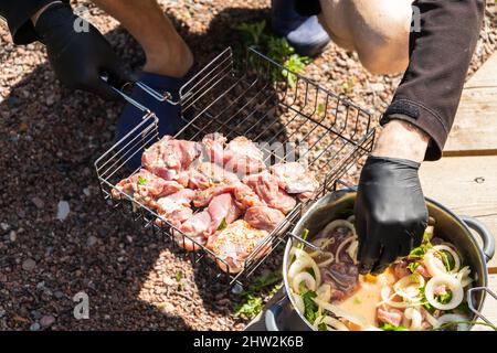 Cottura dello shashlik su una griglia, cuoco stende i cubetti marinati di carne di tacchino in griglia metallica Foto Stock