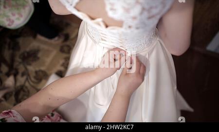 La madre aiuta la sposa a indossare un abito da sposa. Scorta. Le mani legano un corset di un abito da sposa. Foto Stock