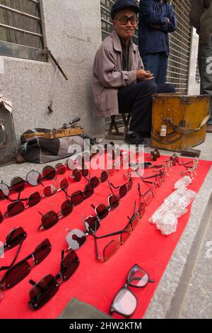 Anziano anziano anziano anziano, oap, pensionato, e venditore di strada di marciapiede, che vende occhiali da sole sulla strada a Tianshui, provincia di Gansu, Cina nord-occidentale. PRC. (125) Foto Stock