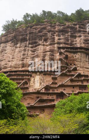 Gradini e passerelle attaccati al fronte roccioso consentono ai visitatori di vedere le antiche statue di argilla di Buddha e divinità buddiste statua attaccata e scolpita nella superficie di pietra della faccia di roccia. Le Grotte di Maijishan, precedentemente romanizzate come Maichishan, Sono una serie di 194 grotte tagliate sul lato della collina di Majishan a Tianshui, provincia di Gansu, Cina PRC. (67/125) Foto Stock