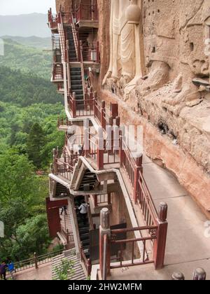 Gradini e passerelle attaccati al fronte roccioso consentono ai visitatori di vedere le antiche statue di argilla di Buddha e divinità buddiste statua attaccata e scolpita nella superficie di pietra della faccia di roccia. Le Grotte di Maijishan, precedentemente romanizzate come Maichishan, Sono una serie di 194 grotte tagliate sul lato della collina di Majishan a Tianshui, provincia di Gansu, Cina PRC. (67/125) Foto Stock