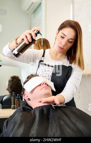 Parrucchiere mettere un asciugamano caldo sul viso dell'uomo prima di rasarlo al barbiere Foto Stock