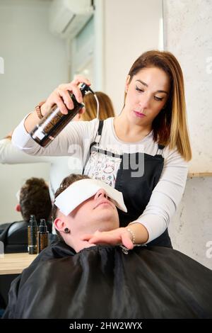 Parrucchiere mettere un asciugamano caldo sul viso dell'uomo prima di rasarlo al barbiere Foto Stock