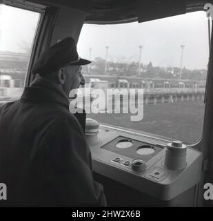 1960s, storico, un driver della metropolitana in berretto e giacca, seduto nella cabina del conducente di un treno della metropolitana di Londra, Londra, Inghilterra, Regno Unito. Noti come stock del 1967, i treni operarono per la prima volta sulla linea Victoria, aperta di recente, nel 1968 e furono in uso fino al 2011. Dotati del sistema Automatic Train Operation (ATO), sono stati i primi treni ferroviari automatici al mondo. Sono stati anche il primo materiale rotabile della metropolitana di Londra a presentare finestre avvolgenti nella cabina del conducente. Foto Stock