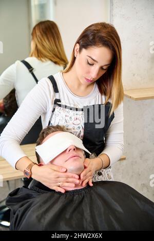 Parrucchiere mettere un asciugamano caldo sul viso dell'uomo prima di rasarlo al barbiere Foto Stock