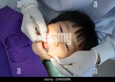 Mano del dentista medico sta lavorando sui denti del bambino asiatico piccolo 6 anni paziente in clinica dentale Foto Stock