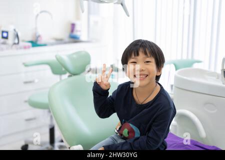 Il ragazzo asiatico si sente felice di sedersi sulla sedia dentale in clinica dentale Foto Stock