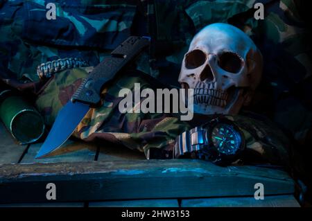 Composizione militare con un cranio e un coltello su una scatola militare. Box militare e uniforme militare. Vista frontale. Foto Stock