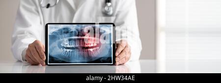 Sezione centrale della mano del medico maschile che mostra schermo bianco vuoto laptop su scrivania Foto Stock