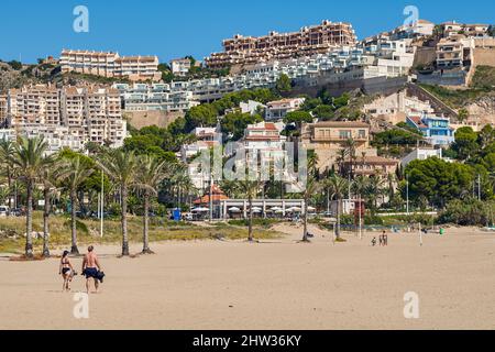 Persone che prendono il sole con i loro ombrelloni sulla sabbia e fanno il bagno nella Platja de l'Illa della città costiera di Cullera, provincia di Valencia, Spagna; Foto Stock