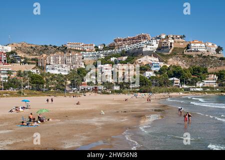 Persone che prendono il sole con i loro ombrelloni sulla sabbia e fanno il bagno nella Platja de l'Illa della città costiera di Cullera, provincia di Valencia, Spagna; Foto Stock