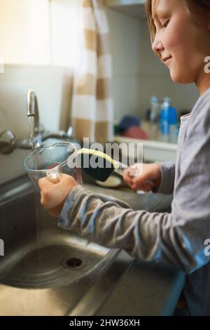 I piatti saranno puliti e squeaky quando sono fatto. Scatto corto di una giovane ragazza lavando piatti a casa. Foto Stock