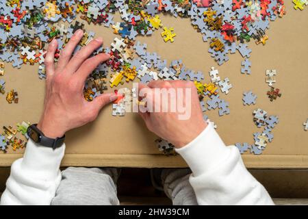 Mano di un giovane ragazzo cercando di risolvere un puzzle, sta mettendo insieme i piccoli pezzi in vari settori. Concetto di intrattenimento. Foto Stock