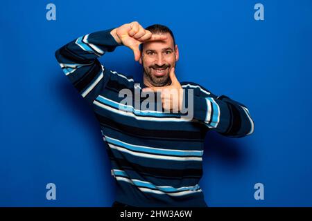 Allegro uomo divertente in abiti casual posa isolato su sfondo blu parete, ritratto studio. Persone Candid emozioni stile di vita concetto. Copia simulata Foto Stock