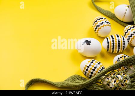 Uova dorate, nere, bianche in una borsa a corda su sfondo giallo. Vista dall'alto. Carta di Pasqua con spazio per la copia del testo Foto Stock