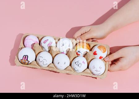 Le mani dei bambini tengono le uova di Pasqua dipinte su uno sfondo rosa. Concetto minimo. Vista dall'alto. Spazio di copia. Foto Stock