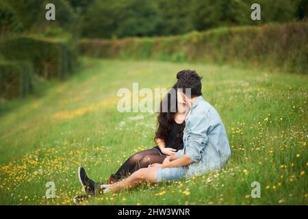 Romanticismo primaverile. Carino giovane coppia seduta in un campo primavera baciare. Foto Stock
