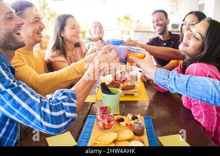 Persone multiculturali che hanno la prima colazione bere caffè e Grazie. Buon divertimento comunitario in un bar con terrazza. Divertente gruppo di amici ridendo e. Foto Stock