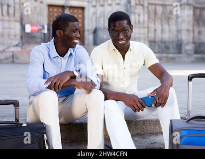 I viaggiatori afroamericani sono gentili a parlare mentre si siedono sulla strada della città Foto Stock