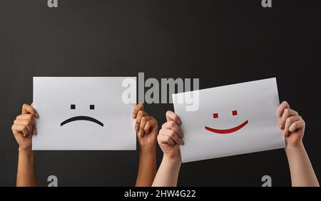 Felice e triste. Scatto di due persone che tengono un cartello con sorrisi felici e tristi su sfondo scuro. Foto Stock