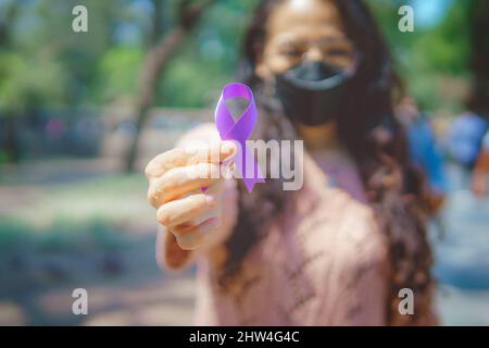 Donna in strada che tiene un nastro viola nella consapevolezza del cancro testicolare che è osservato ogni anno in aprile. Foto Stock
