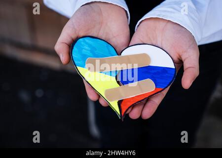 Bandiere ucraine e russe insieme in cuore rotto nelle mani del bambino. Concetto di fine della guerra in Ucraina e riconciliazione Foto Stock