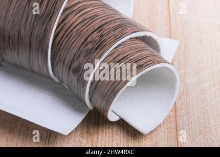 Linoleum. Rotolo di linoleum su sfondo nero. Rivestimenti per pavimenti. Posa di rivestimenti per pavimenti. Tessitura di legno su un rotolo. Il campione viene arrotolato. Foto Stock