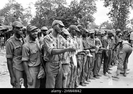 Un grande gruppo di soldati Biafran si è visto qui durante il conlifct, alcuni facendo una pausa per un po' di cibo. 11th giugno 1968 la guerra civile nigeriana, nota anche come guerra di Biafran, durò due anni e mezzo, dal 6 luglio 1967 al 15 gennaio 1970, e fu combattuta per contrastare la secessione di Biafra dalla Nigeria. Il popolo indigeno Igbo di Biafra sentì di non poter più coesistere con il governo federale dominato dal nord a seguito dell'indipendenza dalla Gran Bretagna. Le tensioni politiche, economiche, etniche, culturali e religiose si sono infine follate nella guerra civile dopo il colpo di stato militare del 1966 Foto Stock