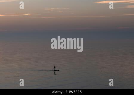 Uomo paddle boarding in mare durante il tramonto Foto Stock