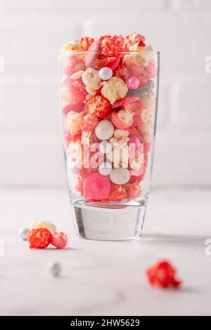 Pop corn rosso e rosa candito colorato con caramelle miste in tazza di vetro Foto Stock