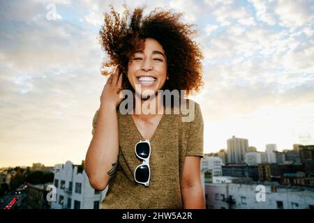 Ritratto di sorridente ragazza ispanica sul tetto urbano al tramonto Foto Stock