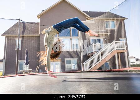 Ragazza (12-13) saltando sul trampolino di fronte a casa Foto Stock