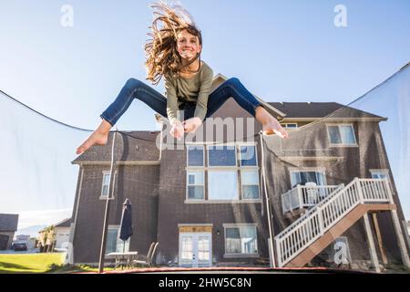 Ragazza (12-13) saltando sul trampolino di fronte a casa Foto Stock