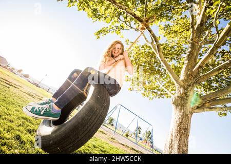 Ragazza sorridente (10-11) su pneumatico swing in giardino Foto Stock