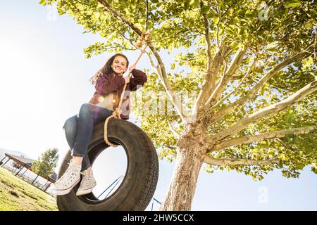 Ragazza sorridente (12-13) su pneumatico swing in giardino Foto Stock