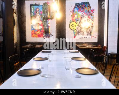 Tavolo da ristorante con dipinti contemporanei sullo sfondo Foto Stock