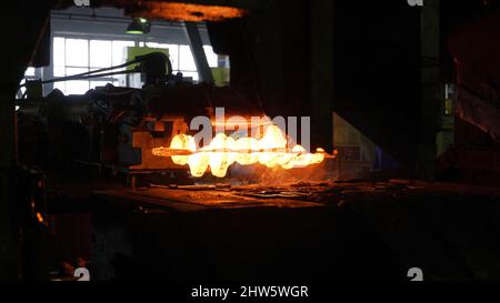 Primo piano del processo di forgiatura del metallo presso la fabbrica. Il martello idraulico forma la billetta calda rossa, la produzione di parti metalliche. Foto Stock