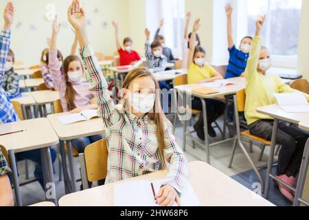 gruppo di studenti in maschere che alzano le mani a scuola Foto Stock