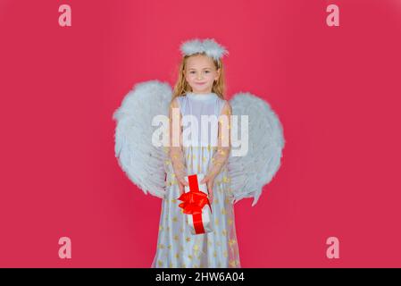 Angelo dei bambini con regalo. Piccolo angelo con ali bianche contiene il regalo. Carino angelo bambina con angeli ali, isolato su rosso. San Valentino Foto Stock