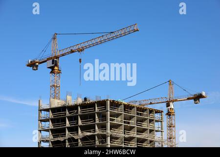 Costruzione torre gru sopra edificio residenziale incompiuto su sfondo cielo blu. Edilizia abitativa, condominio Foto Stock