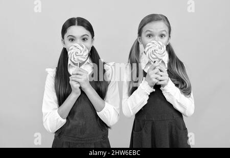 I bambini affamati della scuola tengono i lollipops colorati di swirl sui bastoni sfondo giallo, cibo Foto Stock