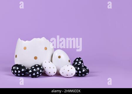 Uova di pasqua bianche e nere con puntini e cuori e coppa d'uovo su sfondo viola Foto Stock