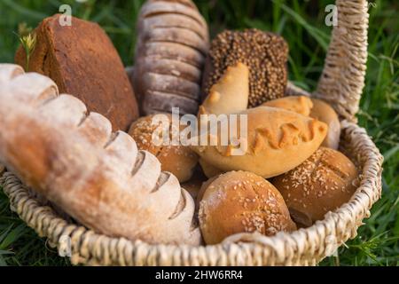 Assorti di gustoso pane fresco e bianco fatto in casa con i semi in cesto di vimini in piedi sul verde erba. Foto di alta qualità Foto Stock