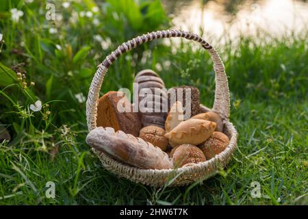 Assorti di gustoso pane fresco e bianco fatto in casa con i semi in cesto di vimini in piedi sul verde erba. Foto di alta qualità Foto Stock