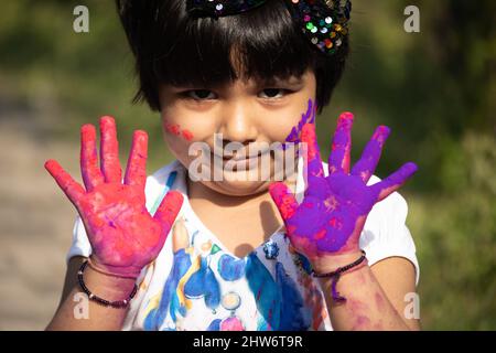 Tema festivo indiano - ragazza felice asiatica del bambino che ha divertimento con la polvere non tossica del colore dell'Holi dell'erbe chiamata Gulal o Abir Rang Aber Foto Stock