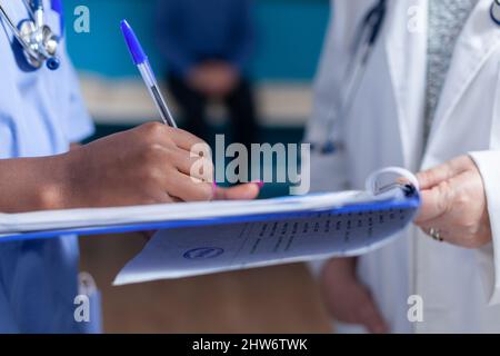 Primo piano dell'infermiera che prende appunti su documenti con l'aiuto del medico in gabinetto sanitario. Assistente medico che firma i file di controllo per l'appuntamento con lo specialista e il paziente. Donna che fa la firma Foto Stock