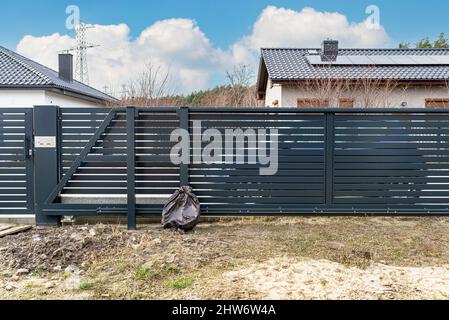 Moderna recinzione in antracite, cancello scorrevole visibile al garage, vista dal giardino. Foto Stock