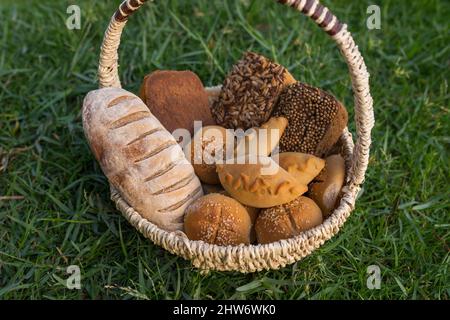 Assorti di gustoso pane fresco e bianco fatto in casa con i semi in cesto di vimini in piedi sul verde erba. Foto di alta qualità Foto Stock