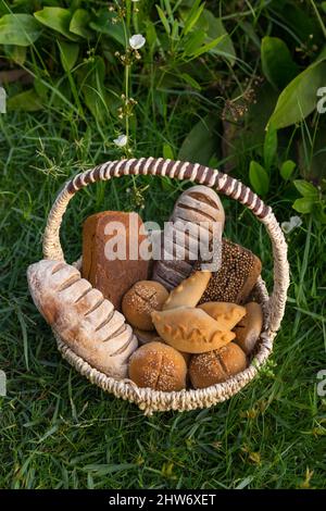 Assorti di gustoso pane fresco e bianco fatto in casa con i semi in cesto di vimini in piedi sul verde erba. Foto di alta qualità Foto Stock